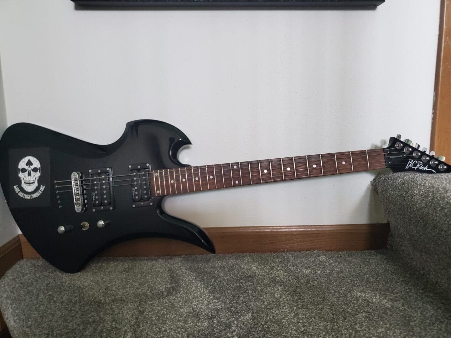 A black electric guitar sitting on the floor.