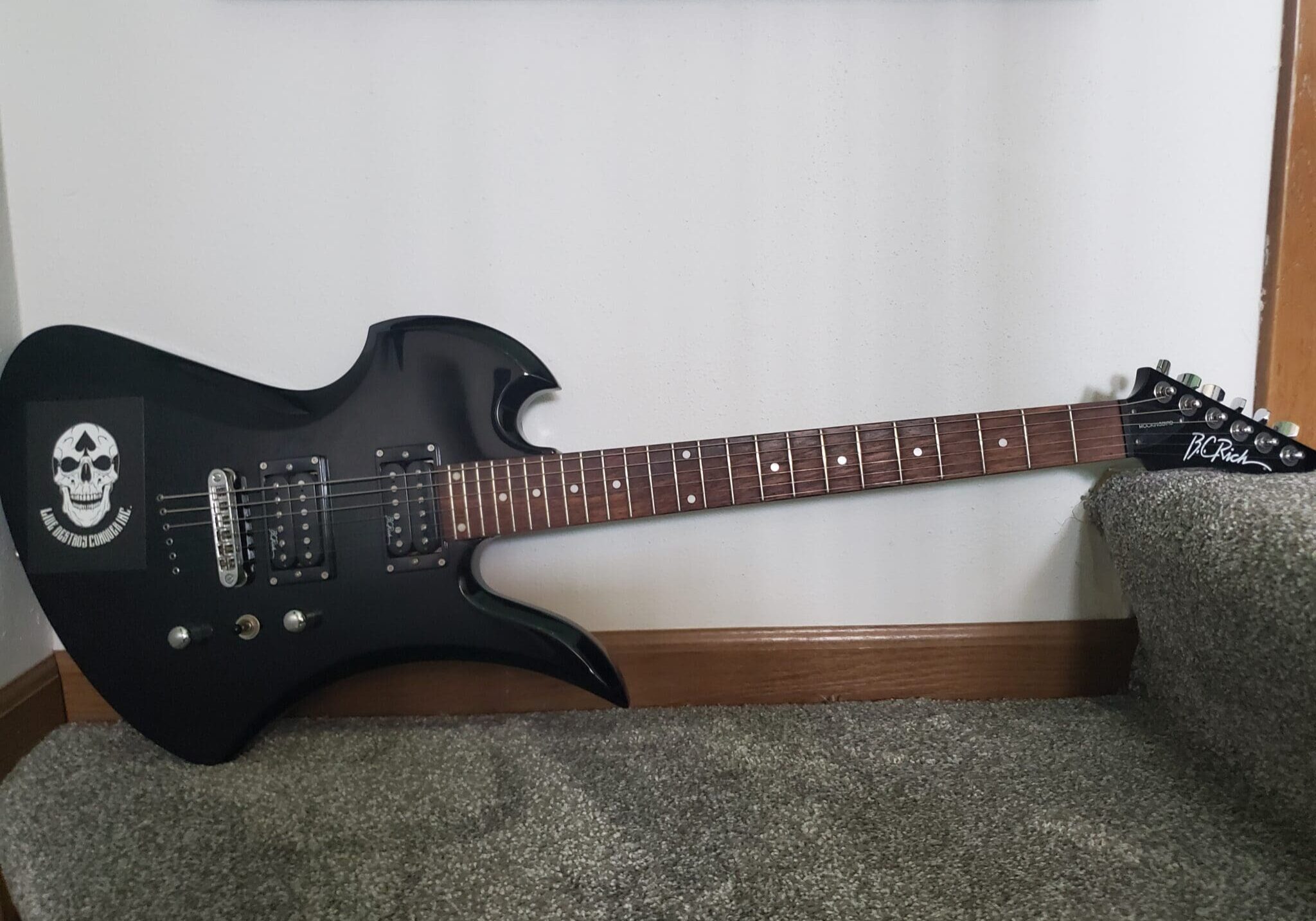 A black electric guitar sitting on the floor.